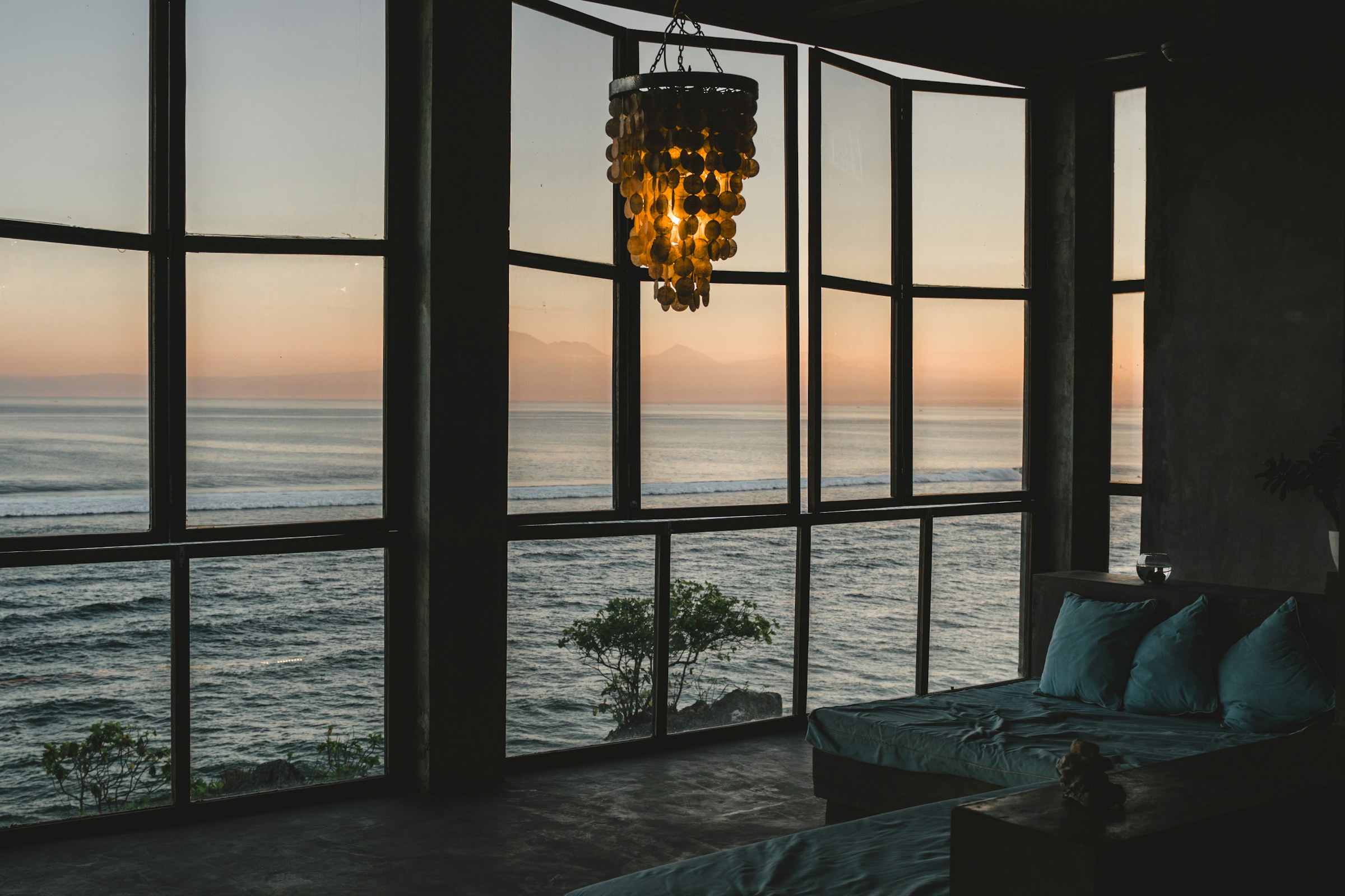 Dim living room at sunset with floor-to-ceiling windows facing the ocean